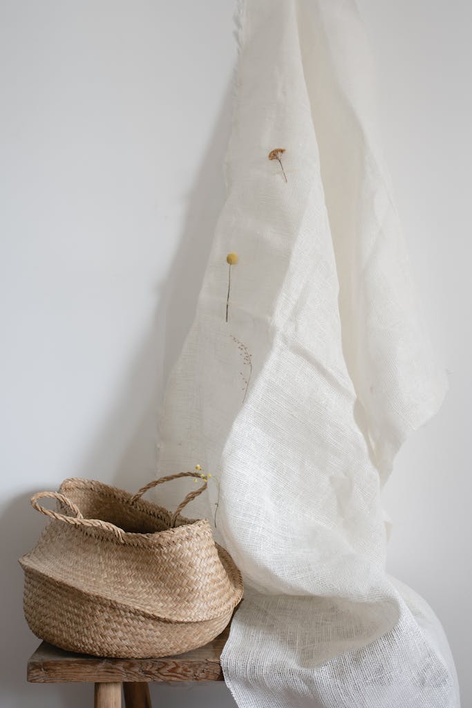 Elegant minimalist composition featuring a wicker basket and white draped fabric with subtle floral accents.